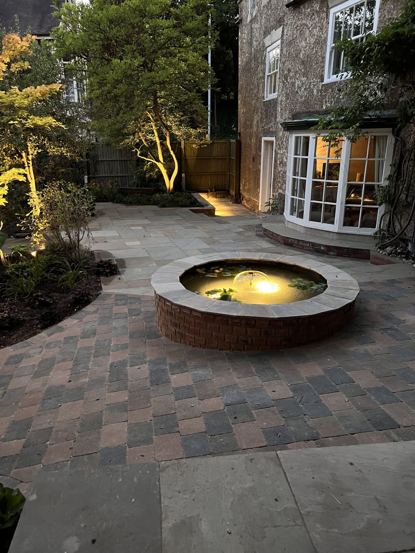 Circular water feature with a submerged light and tree uplighting in a paved garden