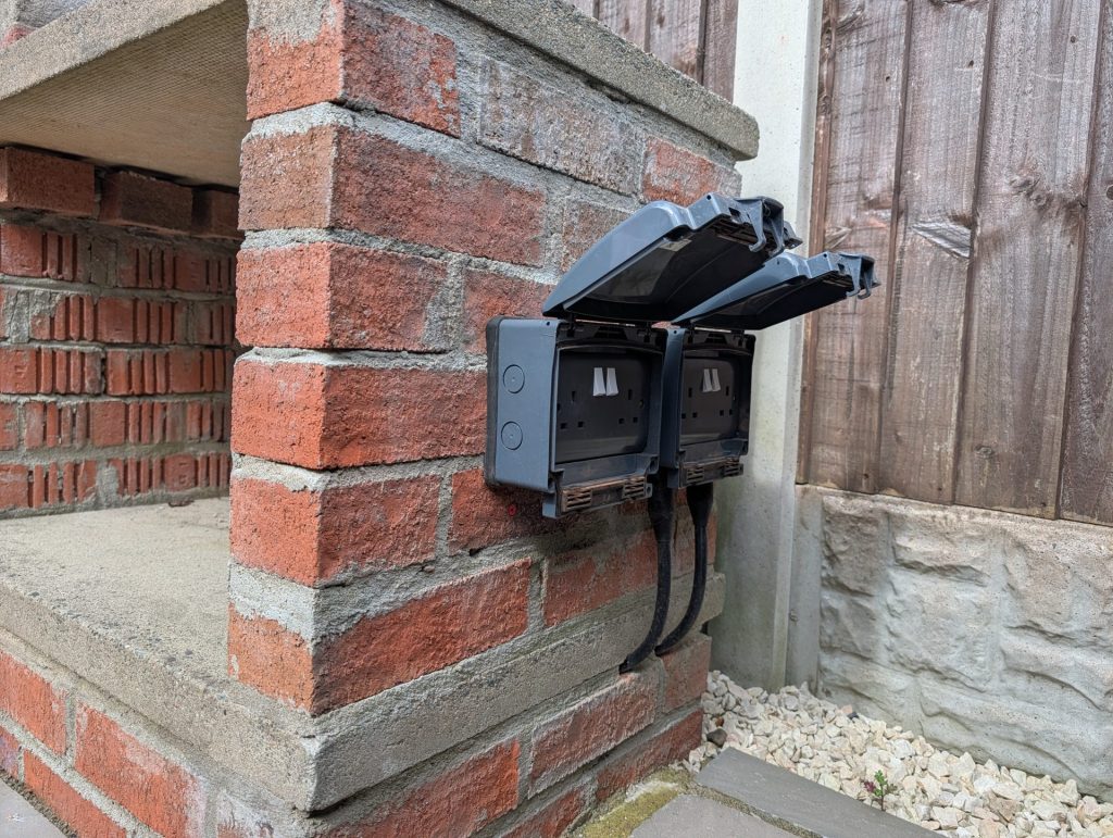 Weatherproof outdoor double socket installed on a brick pillar in a garden